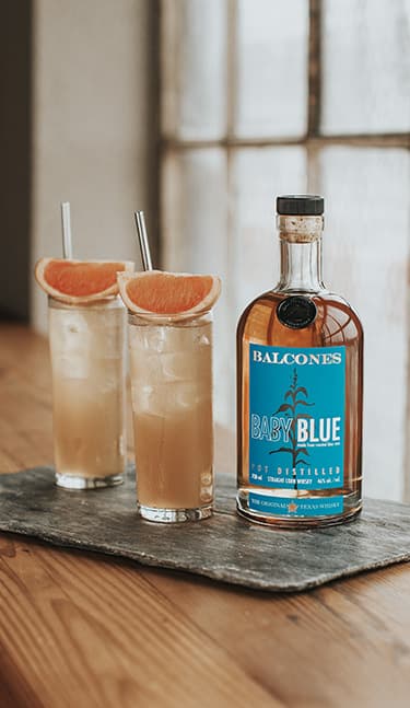 Bottle of Baby Blue Straight Corn Whisky with a glass of baby blue paloma on table