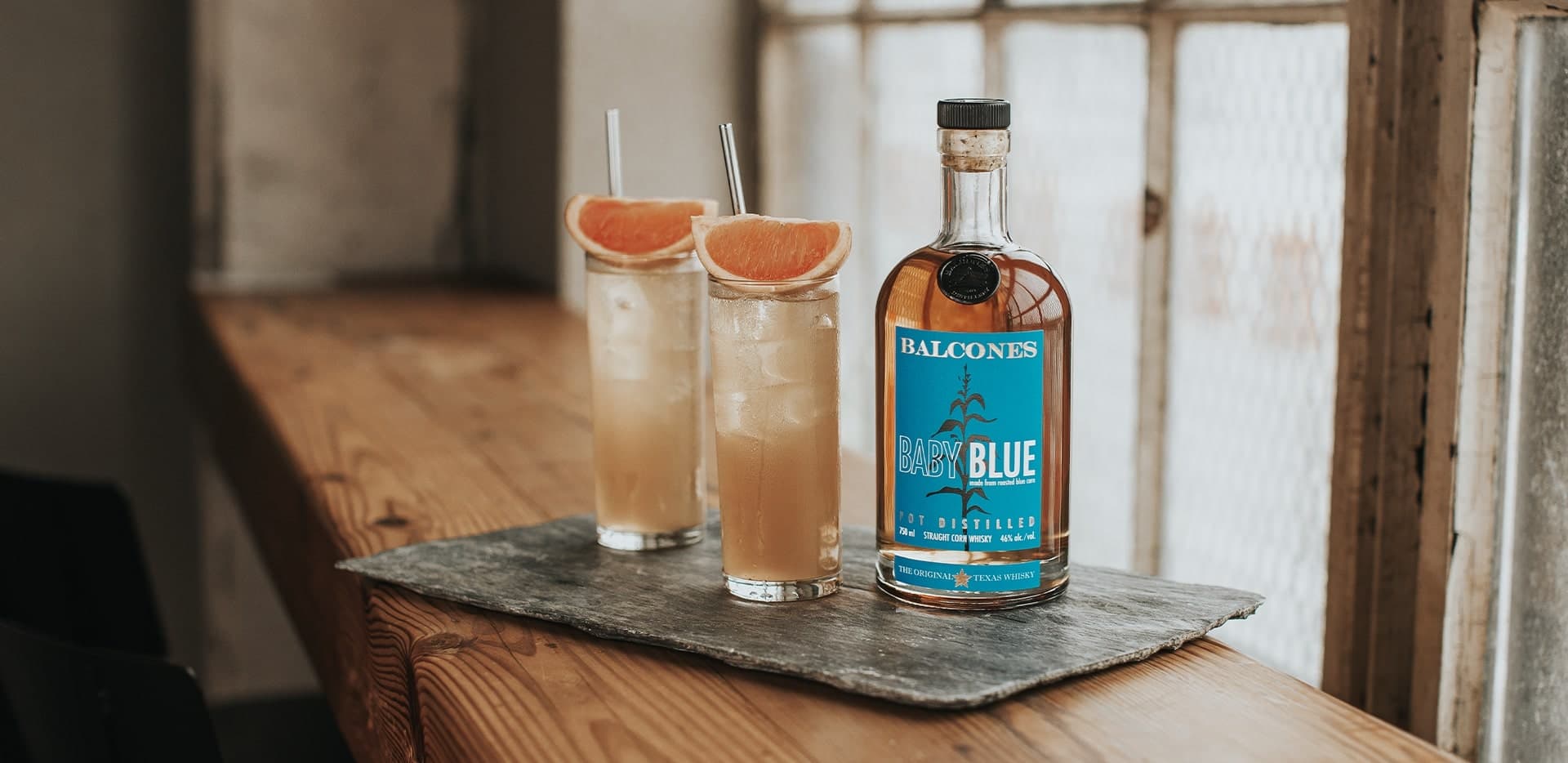 Bottle of Baby Blue Straight Corn Whisky with a glass of baby blue paloma