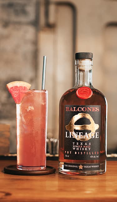 Bottle of Lineage Texas Single Malt Whisky with two glasses of Balcola cocktails on table