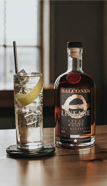 Bottle of Lineage Texas Single Malt Whisky with two glasses of Balcola cocktails on table