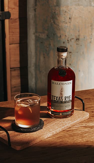 Bottle of Lineage Texas Single Malt Whisky with two glasses of Balcola cocktails on table