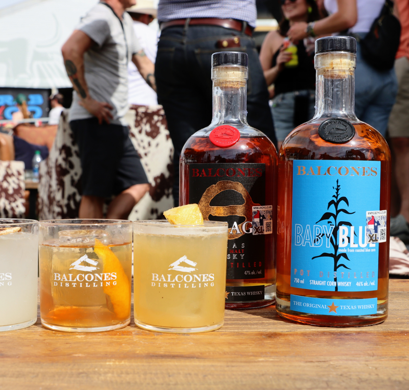 Bottle of Lineage Texas Single Malt Whisky and Baby Blue Straight Corn Whisky with cocktails on bar