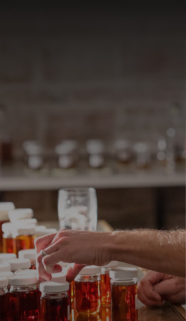 man looking at a bunch of jars of spirits on a workbench
