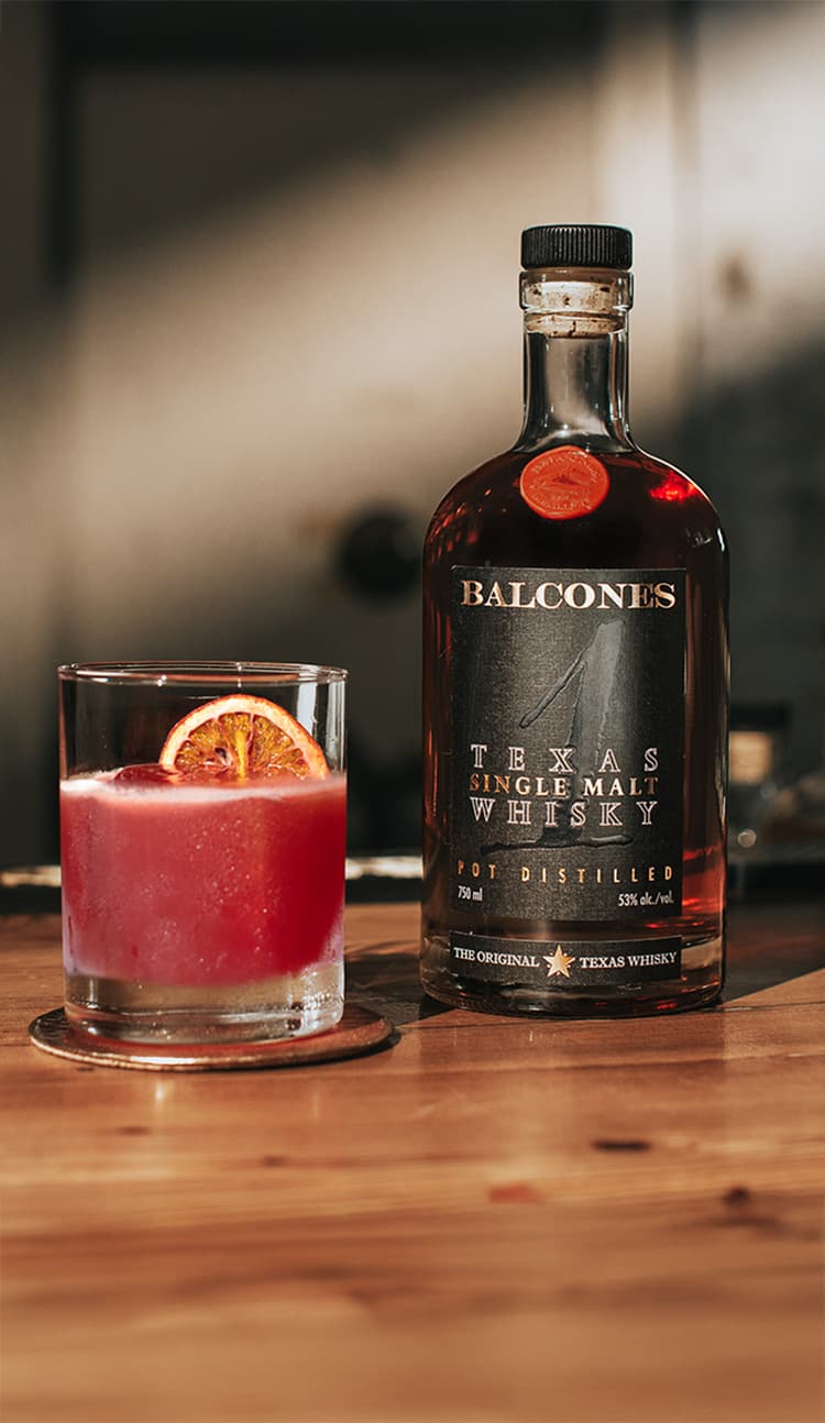 Bottle of Texas 1 Single Malt Whisky with A Cardinal's Message cocktail on a table.