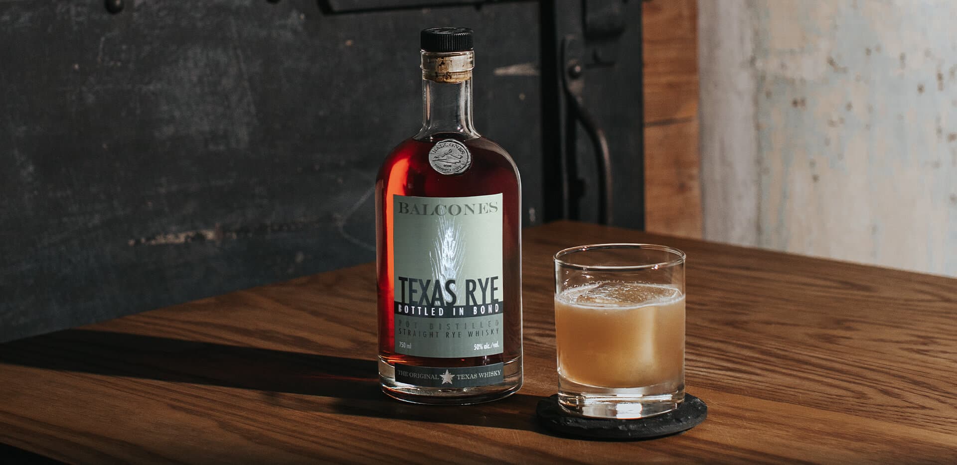 A bottle of Texas Rye Bottled in Bond next to a Banana Sour cocktail on a table.