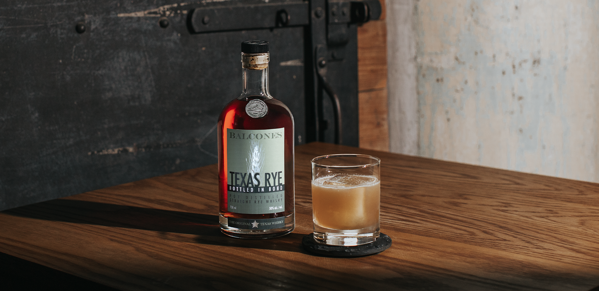 A bottle of Texas Rye Bottled in Bond next to a Banana Sour cocktail on a table.