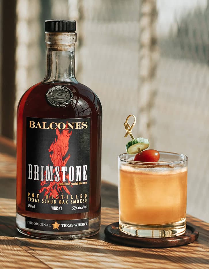 A bottle of Brimstone Smoked Whisky with a Garden Variety cocktail on a table.
