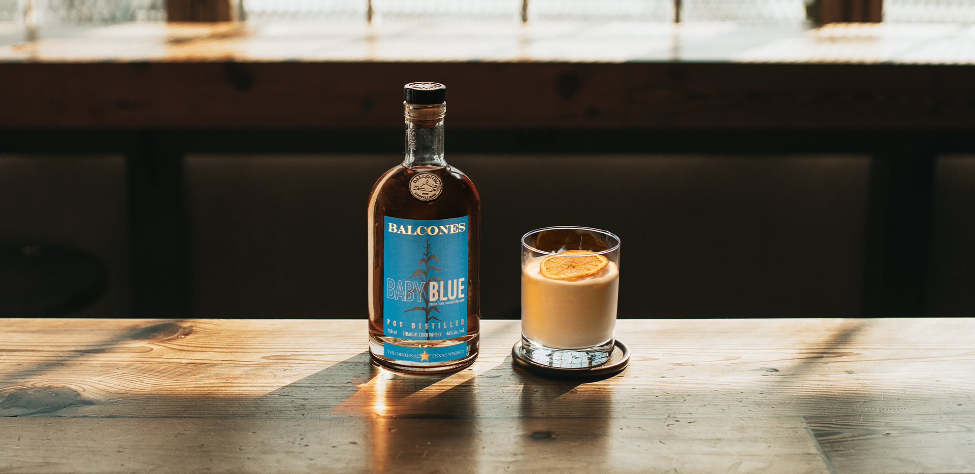 A bottle of Baby Blue Straight Corn Whisky with an It's Orange Dream, Pops cocktail on a table.