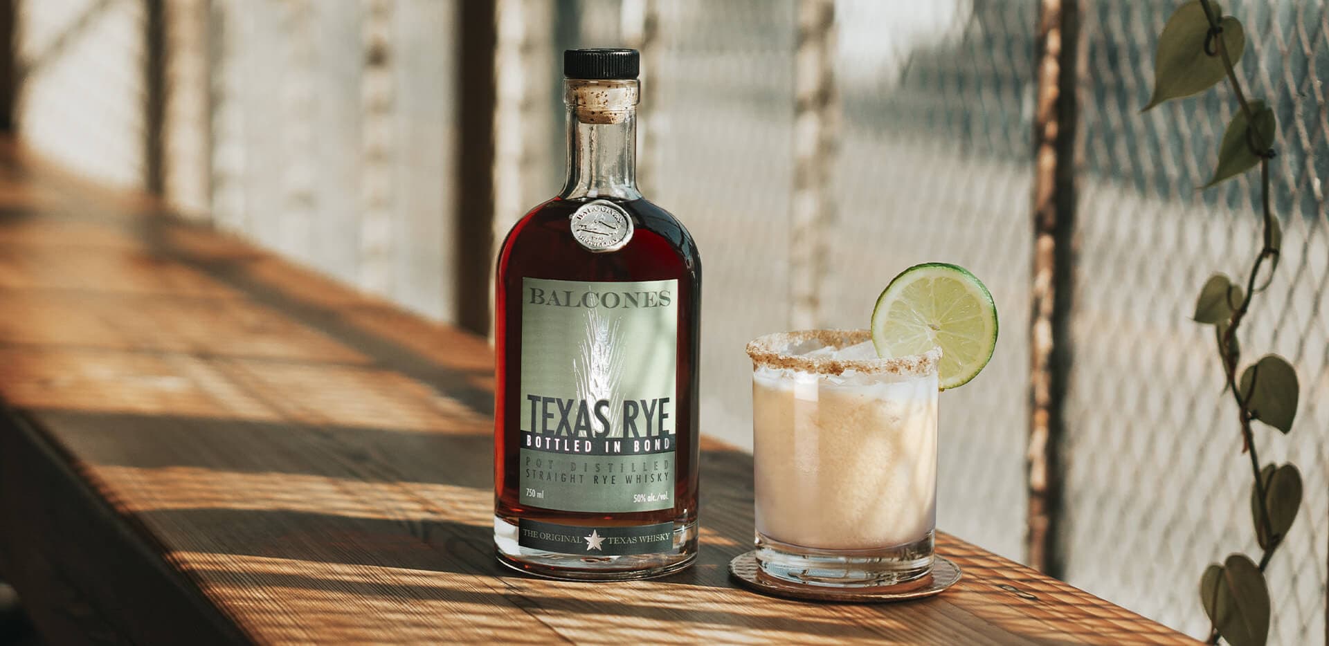 A bottle of Texas Rye Bottled in Bond next to a Key Lime Rye cocktail on a table.