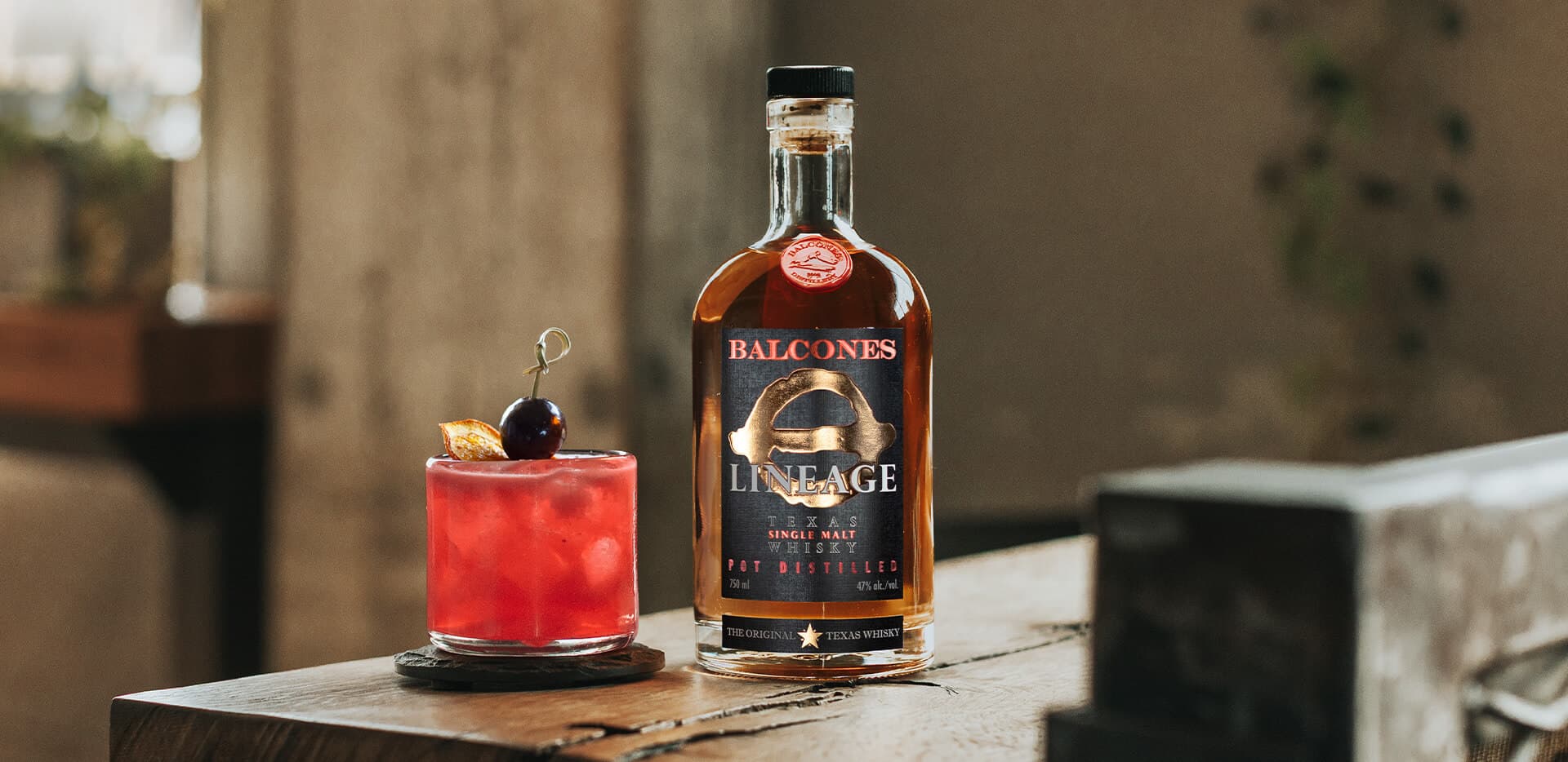 A bottle of Lineage Texas Single Malt Whisky with a Raspberry Fix cocktail on a table.