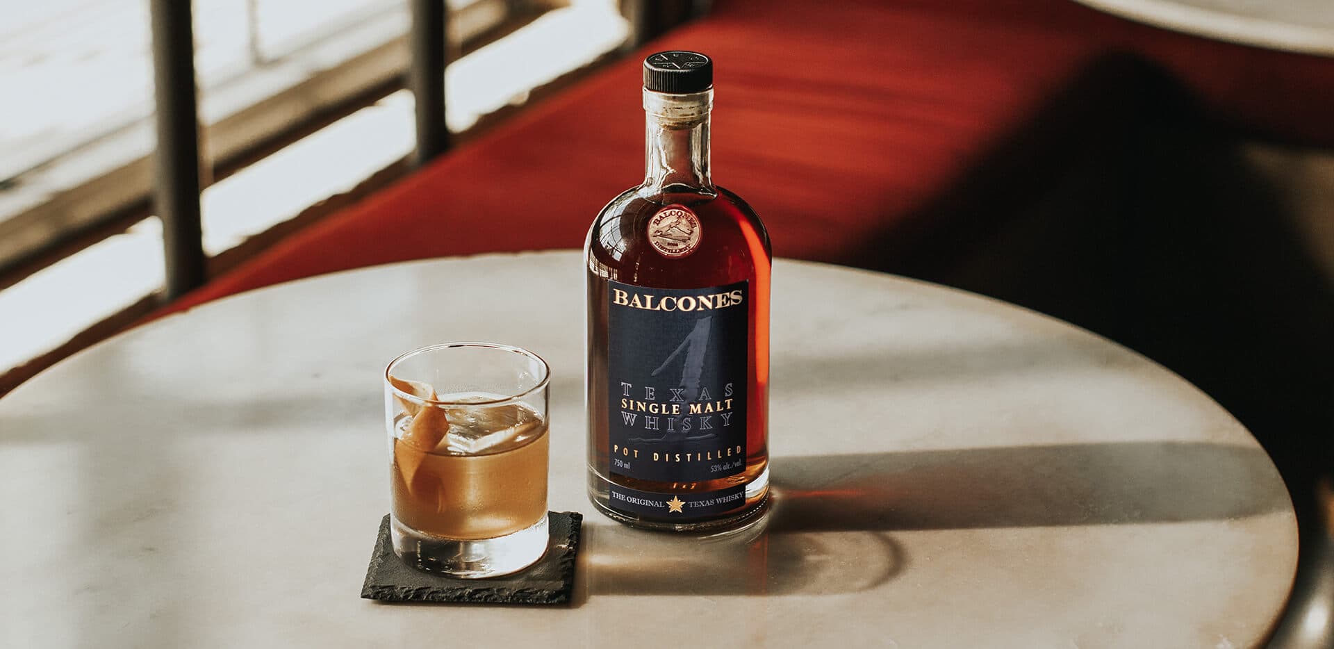 A bottle of Texas 1 Single Malt Whisky with a Texas 1 Old Fashioned cocktail on a table.