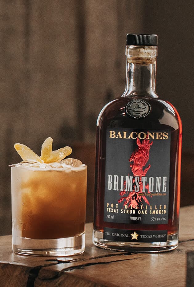 A bottle of Brimstone Smoked Whisky with a Texas Chillin' cocktail on a table.