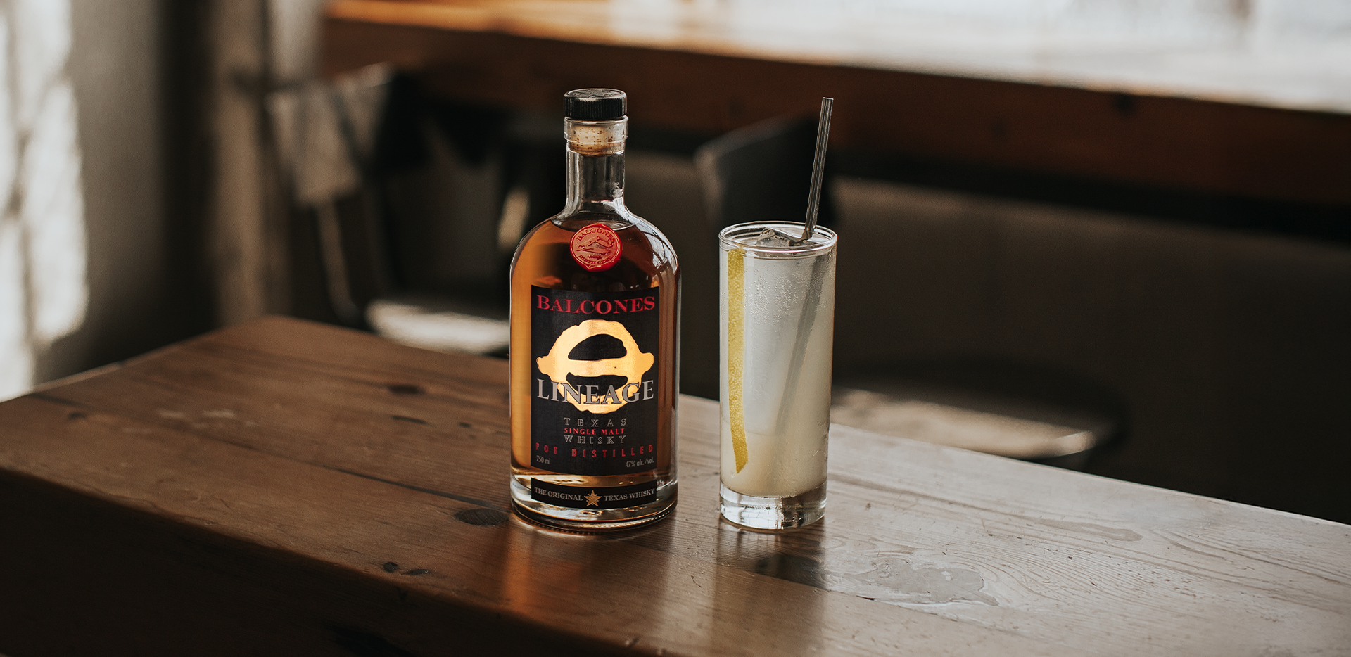Bottle of Lineage Texas Single Malt Whisky with a glass of Texas Collins cocktail on a table.