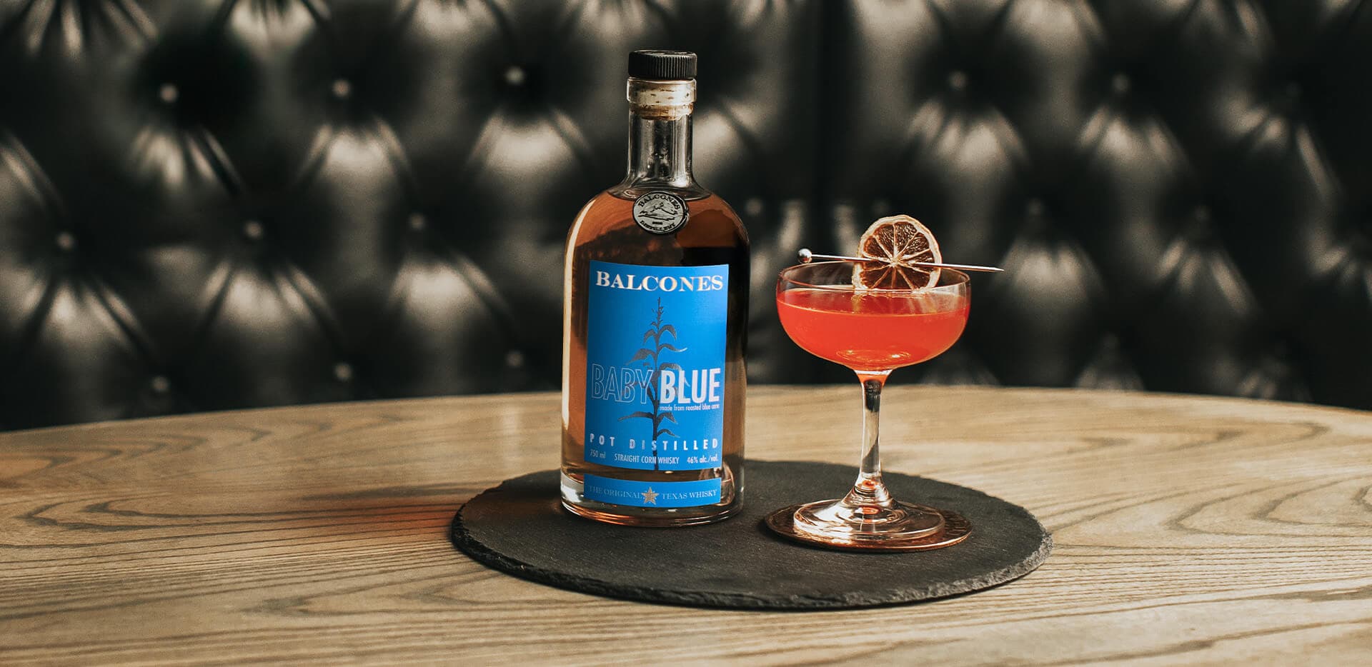 A bottle of Baby Blue Straight Corn Whisky with an It's Orange Dream Pops cocktail on a table.