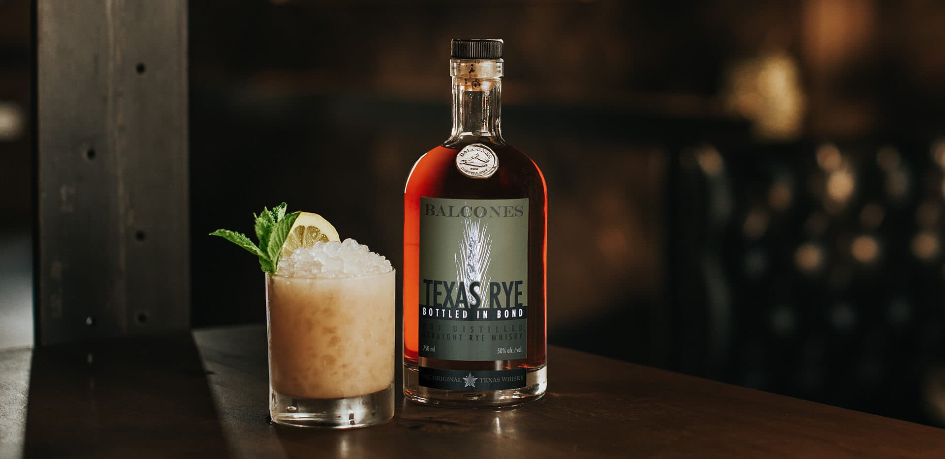 A bottle of Texas Rye Bottled in Bond next to a Texas Rye Tai cocktail on a table.