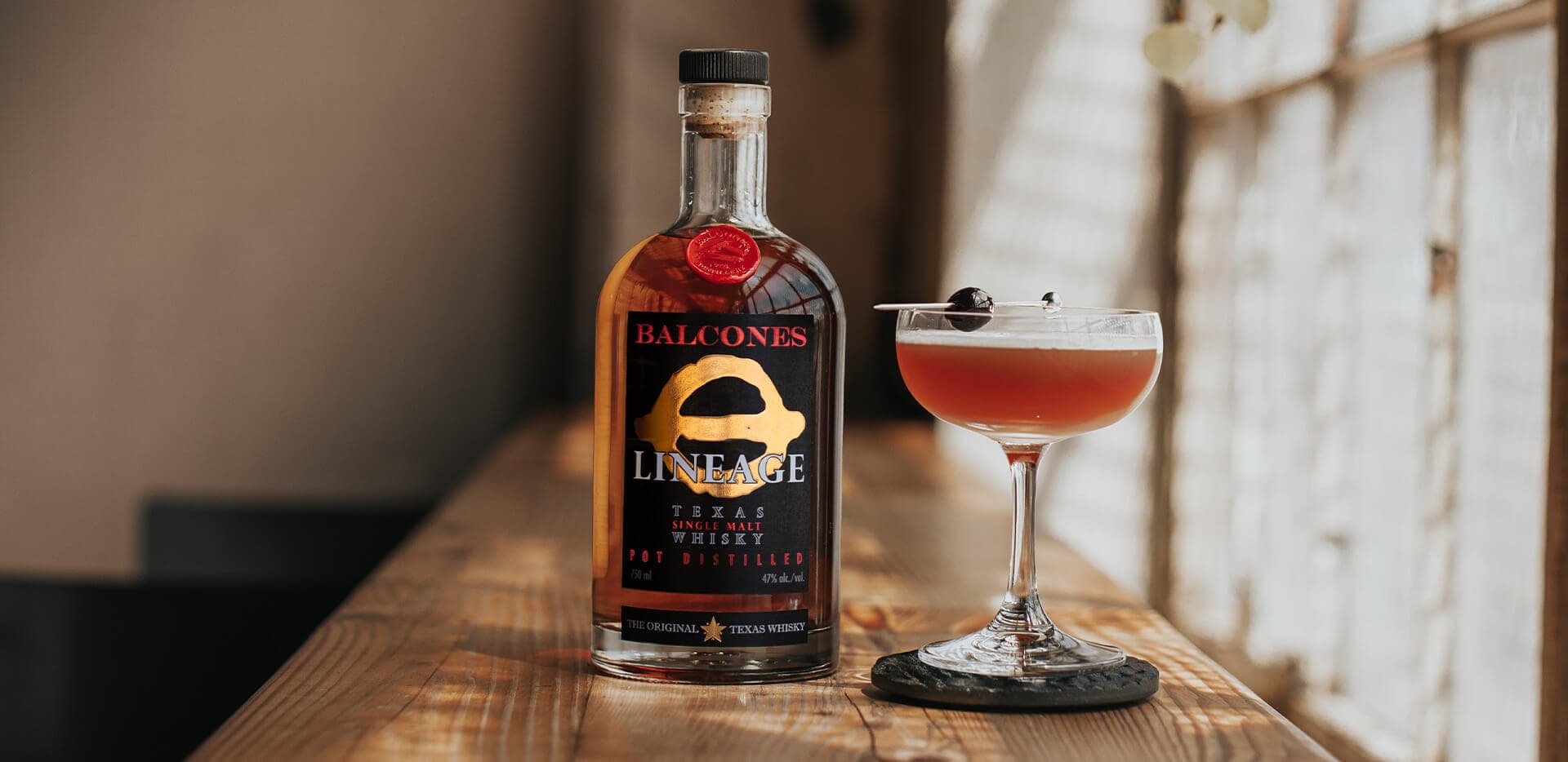 Bottle of Lineage Texas Single Malt Whisky next to Waco Sour cocktail in a martini glass.