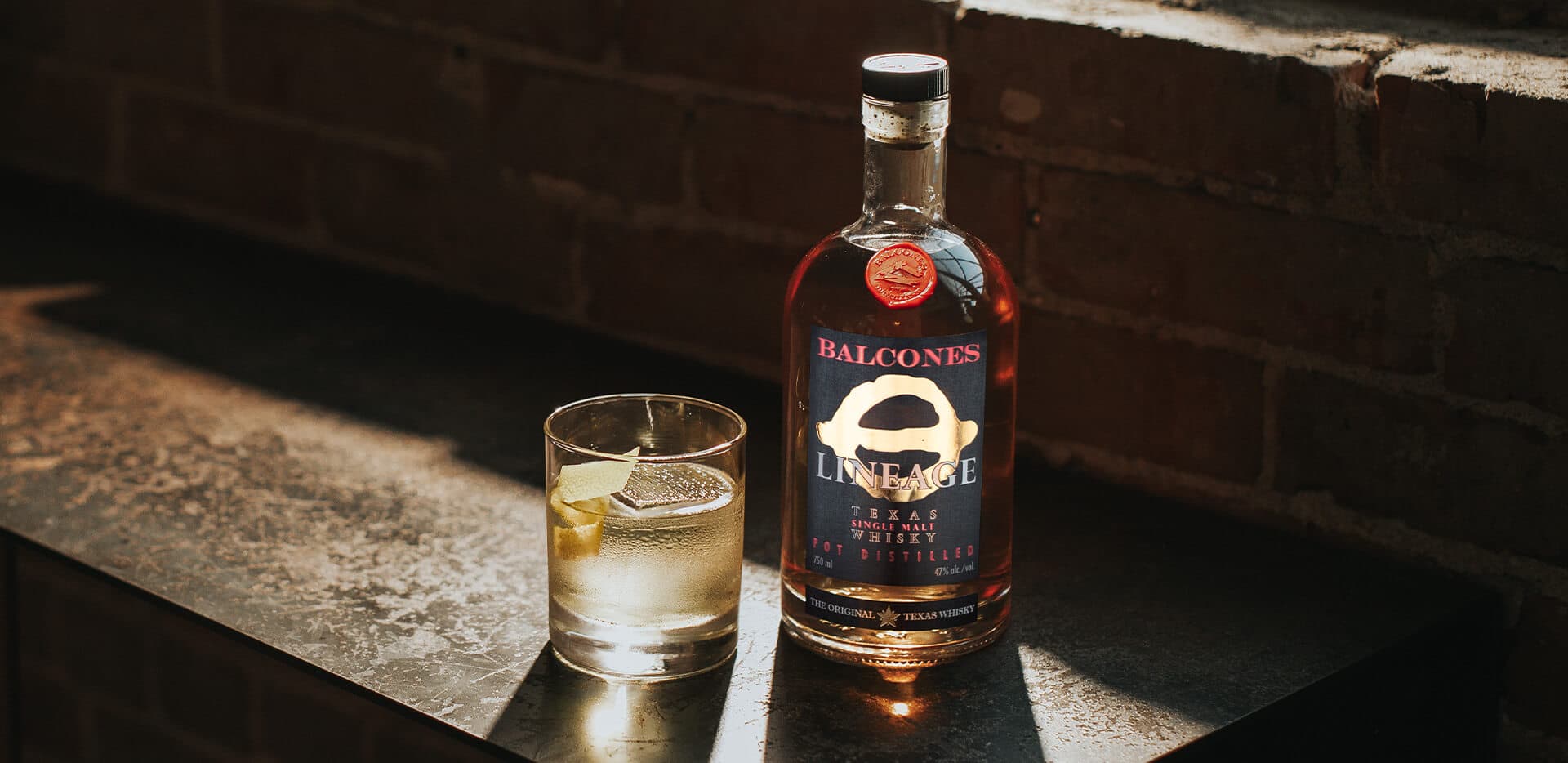 Bottle of Lineage Texas Single Malt Whisky with a glass of White Negroni cocktail on a table.